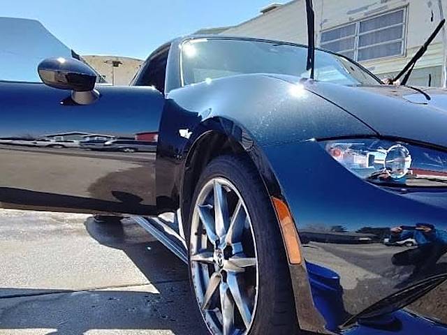 A dark blue Mazda roadster, front three-quarter, door open