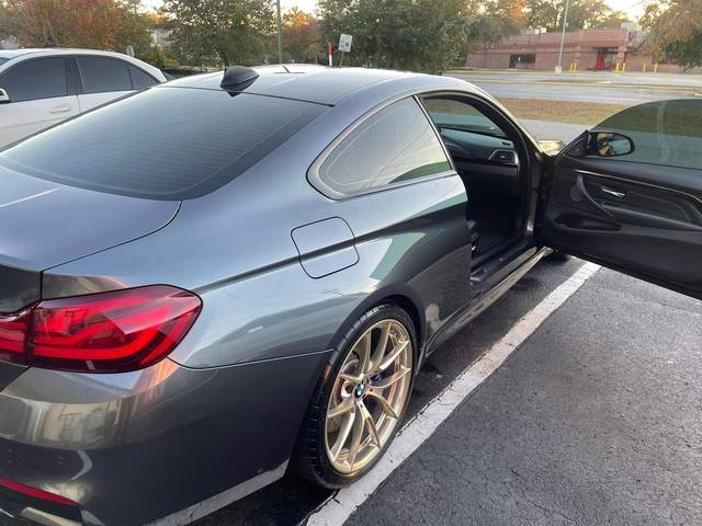 A gray BMW coupe, rear three-quarter, door open